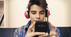 A boy wearing headphones and staring at his phone