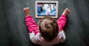 A baby or toddler sits watching a tablet.